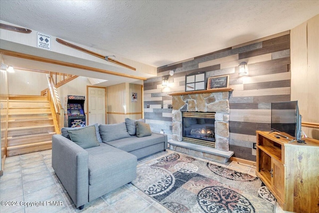 living area with wooden walls, stairway, a textured ceiling, and a stone fireplace