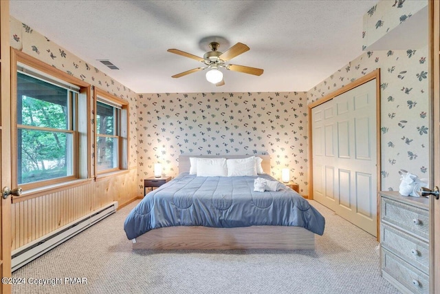 carpeted bedroom featuring wallpapered walls, visible vents, baseboard heating, and a textured ceiling