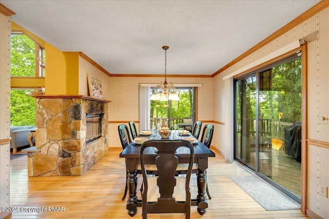 dining area featuring light wood-style flooring, a fireplace, ornamental molding, wallpapered walls, and an inviting chandelier