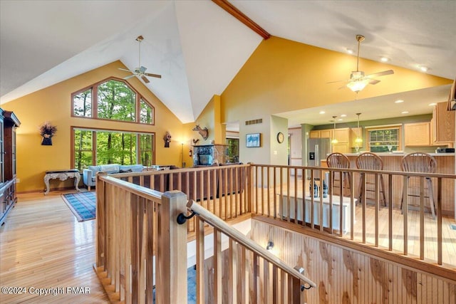 corridor with high vaulted ceiling, light wood finished floors, an upstairs landing, and a healthy amount of sunlight