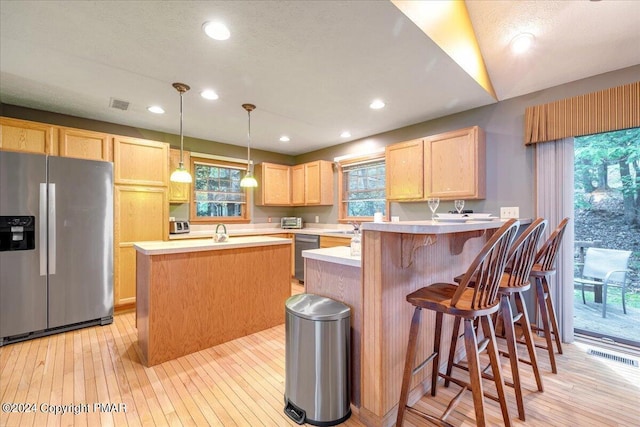 kitchen with stainless steel appliances, a peninsula, light countertops, light brown cabinetry, and light wood finished floors