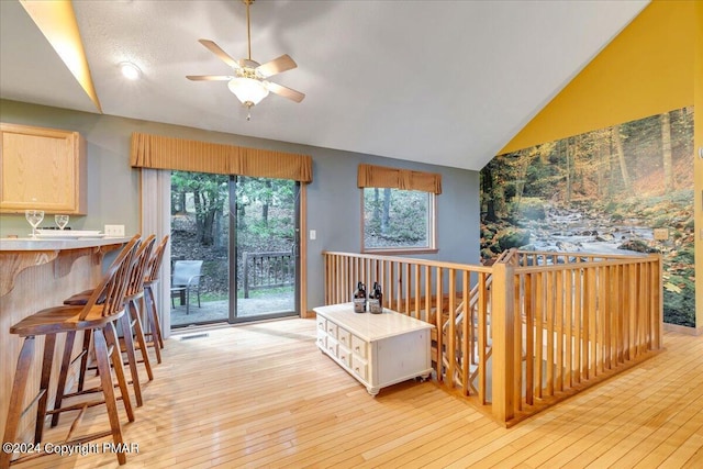 interior space featuring a breakfast bar area, light countertops, vaulted ceiling, ceiling fan, and light wood-type flooring