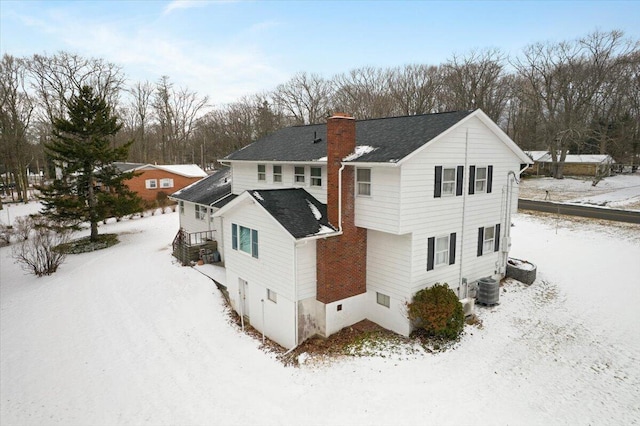 snow covered rear of property with a chimney and central air condition unit