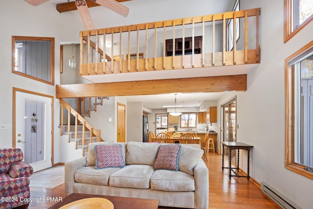 living area featuring light wood-style flooring, a towering ceiling, stairway, baseboard heating, and baseboards