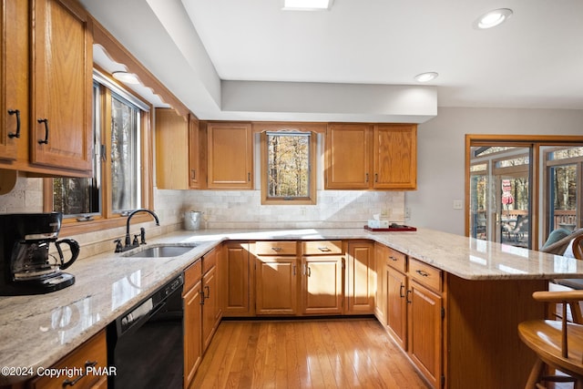 kitchen with black dishwasher, a breakfast bar area, light stone counters, a peninsula, and a sink