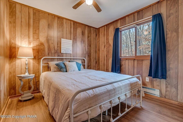 bedroom with a baseboard radiator, wood walls, a ceiling fan, and wood finished floors