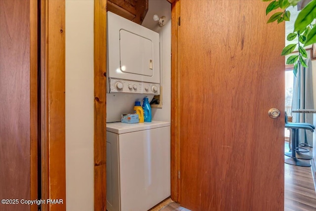laundry room featuring stacked washer / drying machine, wood finished floors, and laundry area