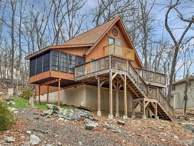 back of property with roof with shingles, a sunroom, a deck, and stairway