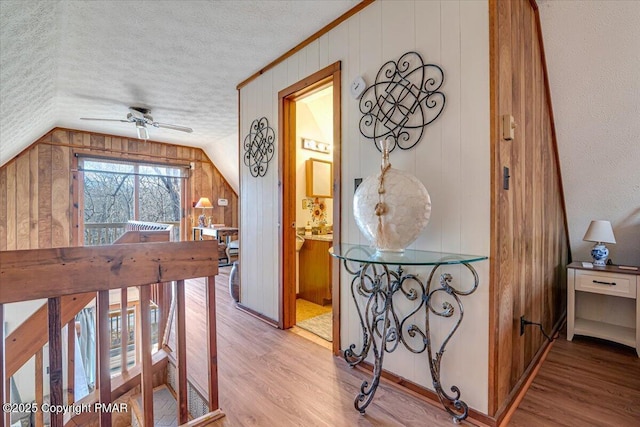 hall with lofted ceiling, wood walls, wood finished floors, and a textured ceiling