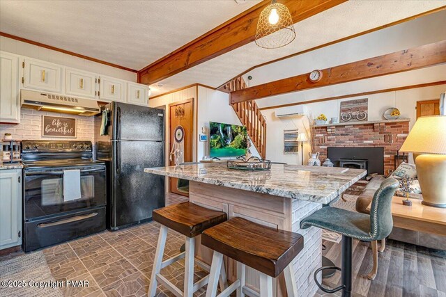 kitchen with a wall mounted air conditioner, under cabinet range hood, beamed ceiling, light stone countertops, and black appliances
