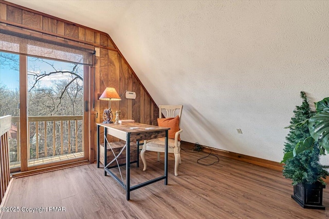 office space featuring a textured ceiling, baseboards, lofted ceiling, wood finished floors, and wood walls
