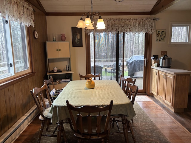 dining area featuring a baseboard heating unit, wood walls, wood finished floors, and a notable chandelier