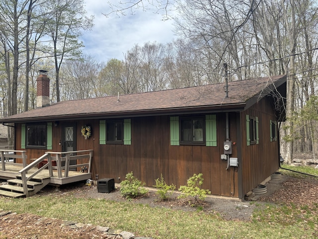 view of front of property featuring roof with shingles, a wooden deck, and a chimney