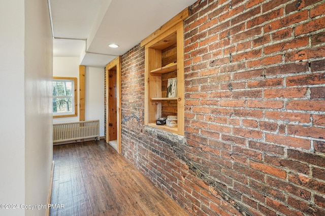 corridor with built in shelves, radiator, wood-type flooring, and brick wall