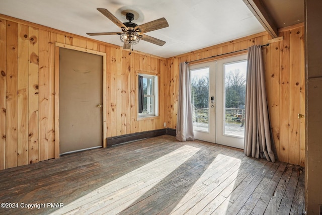 spare room featuring french doors, ceiling fan, wooden walls, and hardwood / wood-style floors