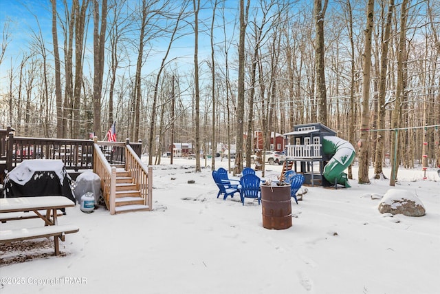 snowy yard featuring a wooden deck and a playground