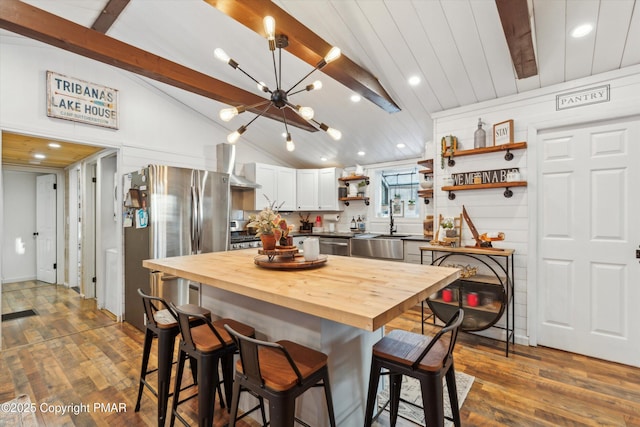 kitchen featuring wooden counters, white cabinetry, a chandelier, lofted ceiling with beams, and wall chimney exhaust hood