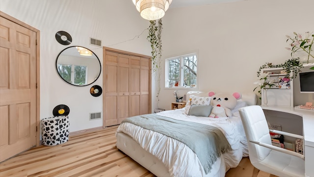 bedroom with light wood-type flooring, visible vents, a high ceiling, and a closet