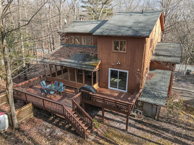 rear view of property with a wooden deck, outdoor dining area, and a shingled roof