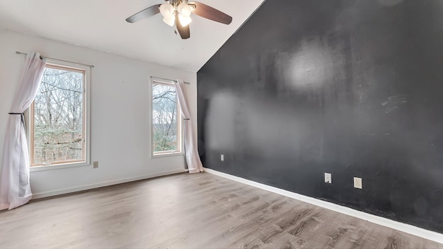 spare room featuring baseboards, plenty of natural light, wood finished floors, and a ceiling fan