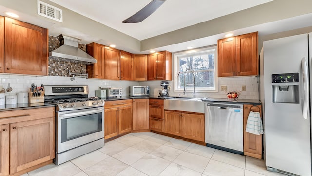 kitchen featuring dark countertops, visible vents, stainless steel appliances, wall chimney exhaust hood, and a sink