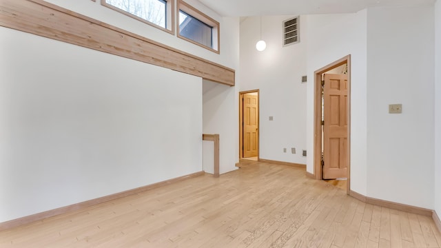 spare room with visible vents, baseboards, a towering ceiling, and light wood finished floors