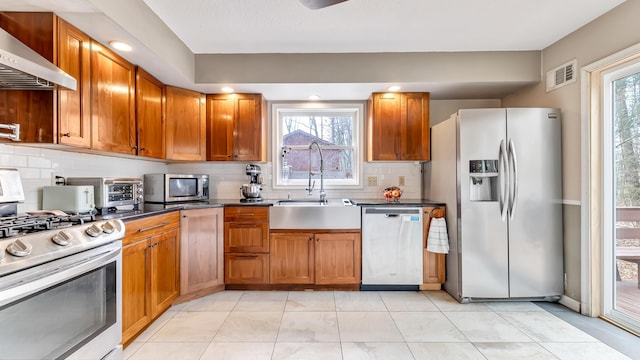 kitchen with visible vents, a sink, dark countertops, appliances with stainless steel finishes, and wall chimney range hood