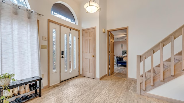 foyer entrance featuring baseboards, stairs, light wood-type flooring, and a towering ceiling