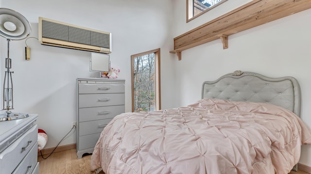 bedroom with light wood-type flooring, baseboards, and an AC wall unit