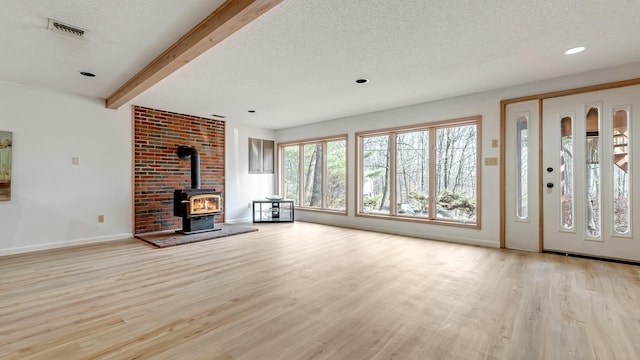 unfurnished living room featuring beam ceiling, a wood stove, wood finished floors, and a textured ceiling