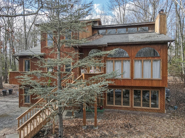 back of property featuring a chimney, stairs, and roof with shingles