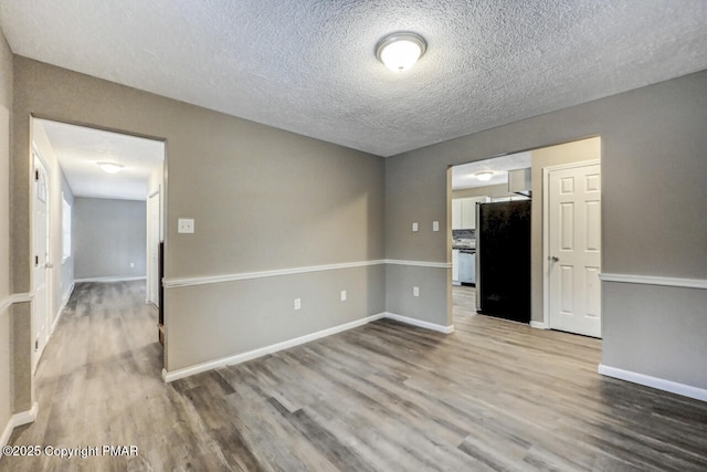 spare room with a textured ceiling, wood finished floors, and baseboards