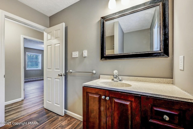 bathroom with a baseboard radiator, baseboards, wood finished floors, and vanity