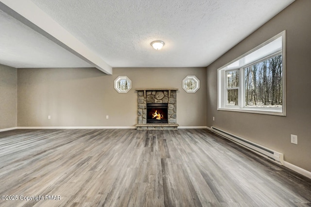 unfurnished living room with a stone fireplace, a textured ceiling, beam ceiling, hardwood / wood-style floors, and a baseboard heating unit