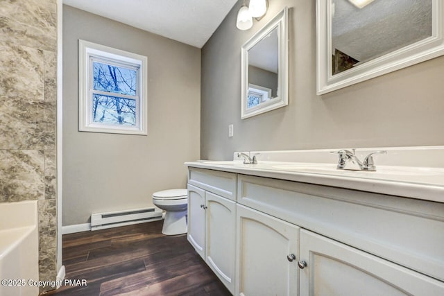 full bathroom with double vanity, toilet, a baseboard heating unit, a sink, and wood finished floors