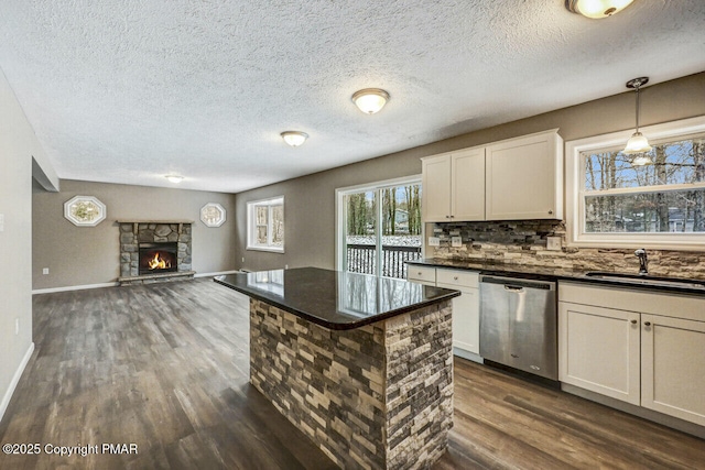 kitchen featuring pendant lighting, sink, dishwasher, white cabinets, and a stone fireplace