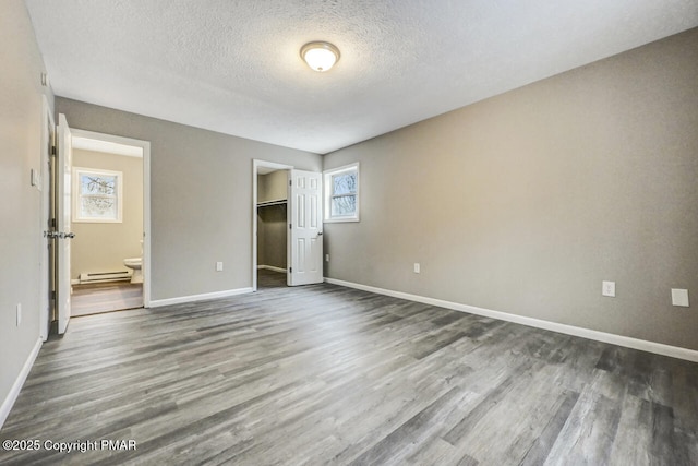 unfurnished bedroom featuring multiple windows, connected bathroom, a closet, and a baseboard heating unit