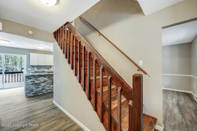 stairway with a textured ceiling, baseboards, and wood finished floors