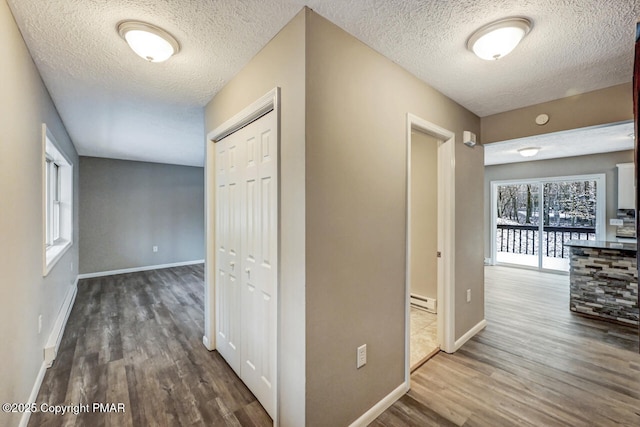 hallway with a textured ceiling, baseboard heating, wood finished floors, and baseboards