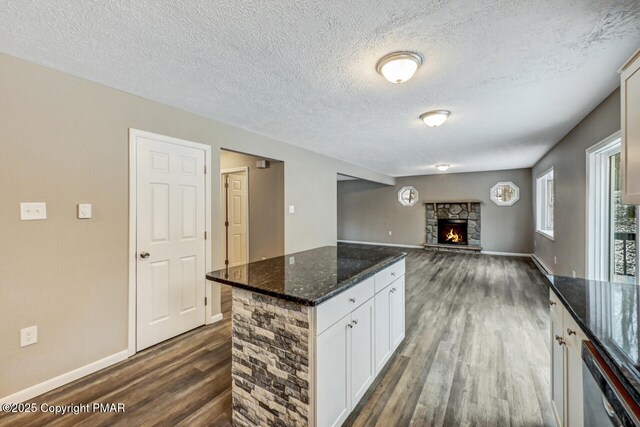 kitchen featuring dark hardwood / wood-style floors, a fireplace, white cabinetry, dishwasher, and dark stone countertops