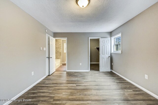 unfurnished bedroom featuring connected bathroom, a spacious closet, a textured ceiling, dark hardwood / wood-style floors, and a closet