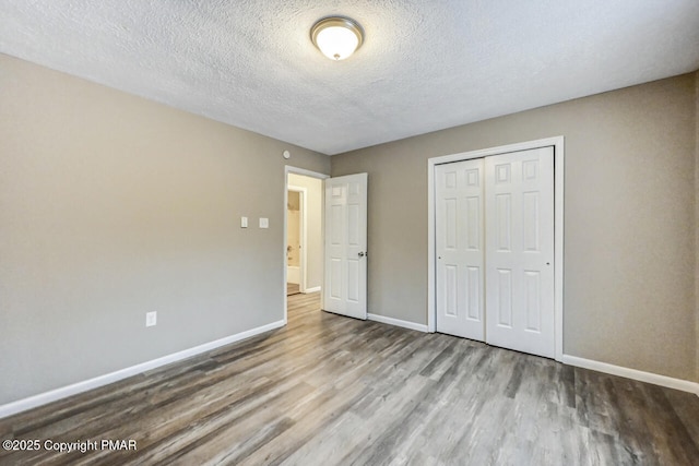 unfurnished bedroom with a closet, a textured ceiling, baseboards, and wood finished floors