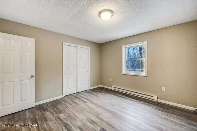 unfurnished bedroom with wood-type flooring, a closet, a textured ceiling, and baseboard heating