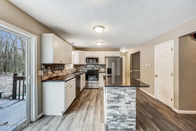 kitchen featuring baseboard heating, white cabinetry, appliances with stainless steel finishes, and decorative light fixtures