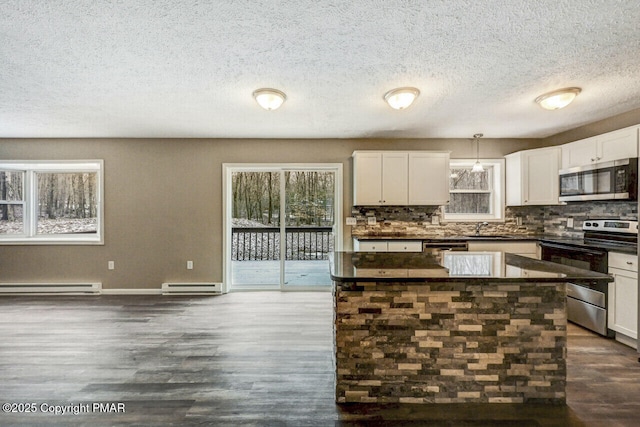 kitchen with dark countertops, plenty of natural light, appliances with stainless steel finishes, and baseboard heating