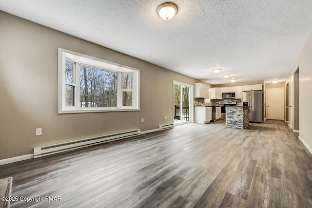 unfurnished living room with a baseboard heating unit, a textured ceiling, wood finished floors, and baseboards