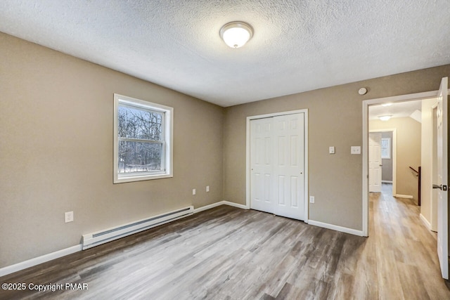 unfurnished bedroom featuring a baseboard radiator, a textured ceiling, light wood-type flooring, and a closet