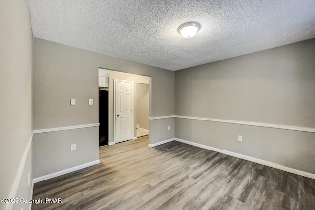 unfurnished room featuring a textured ceiling, baseboards, and wood finished floors