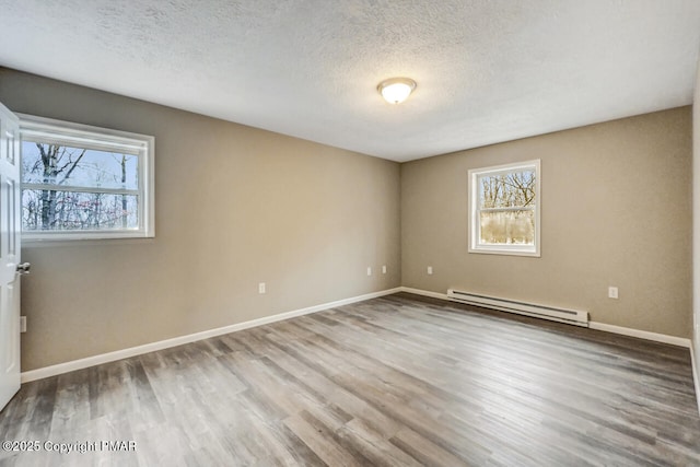 unfurnished room with a baseboard heating unit, wood finished floors, a wealth of natural light, and baseboards