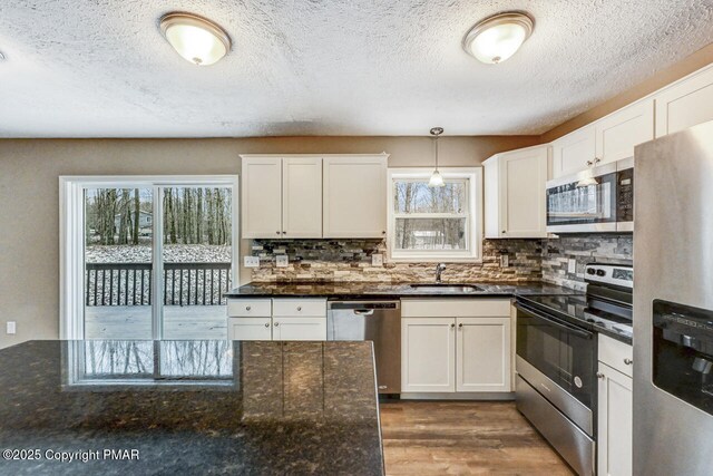 kitchen featuring appliances with stainless steel finishes, white cabinetry, hanging light fixtures, dark stone countertops, and tasteful backsplash